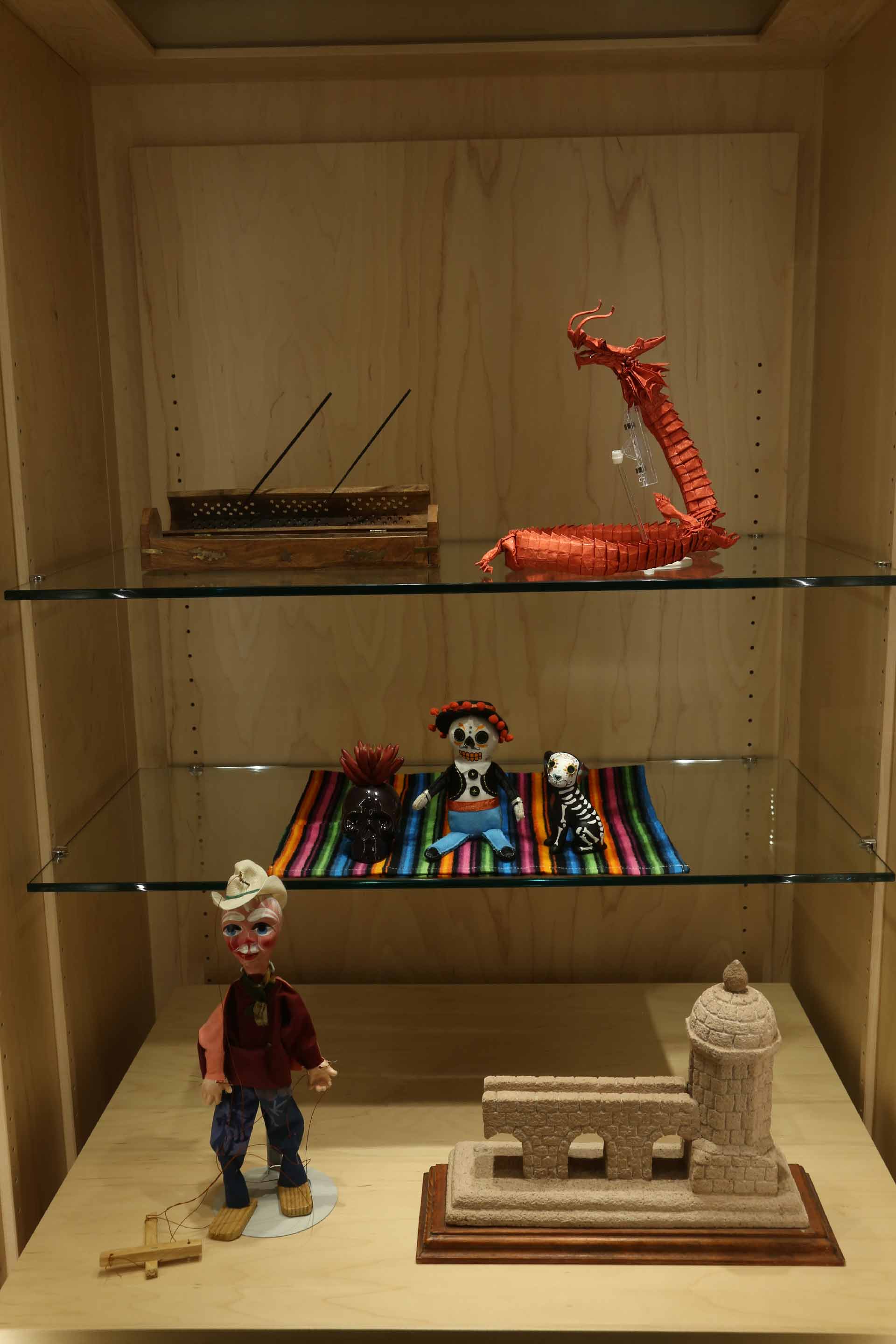 an overview shot of the small brown case, red dragon, skull, figure, dog, puppet doll and building sculpture as they are on display
