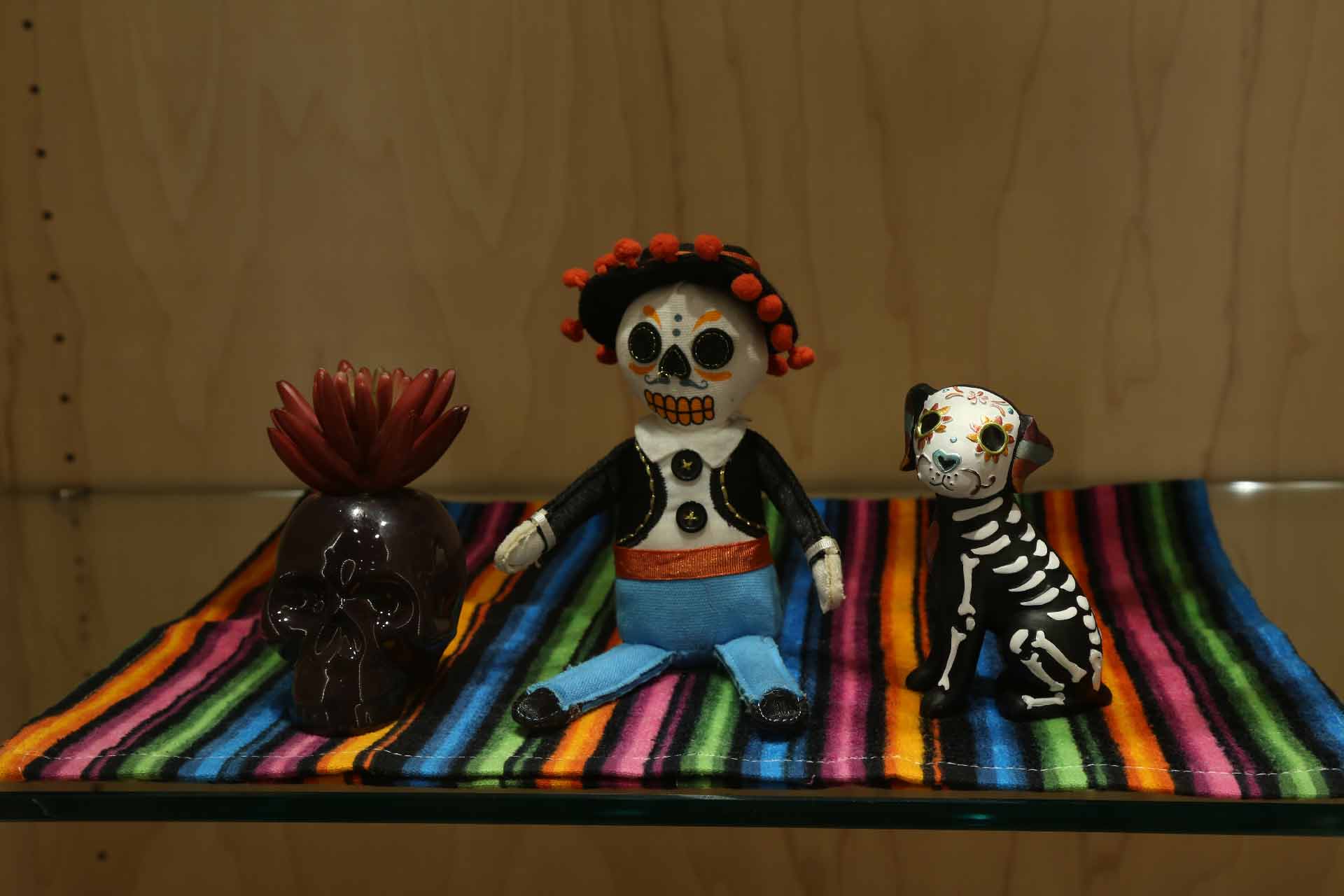 a dark brown skull, small figure, and dog all stylized in skull decoration sitting on a colorful mat