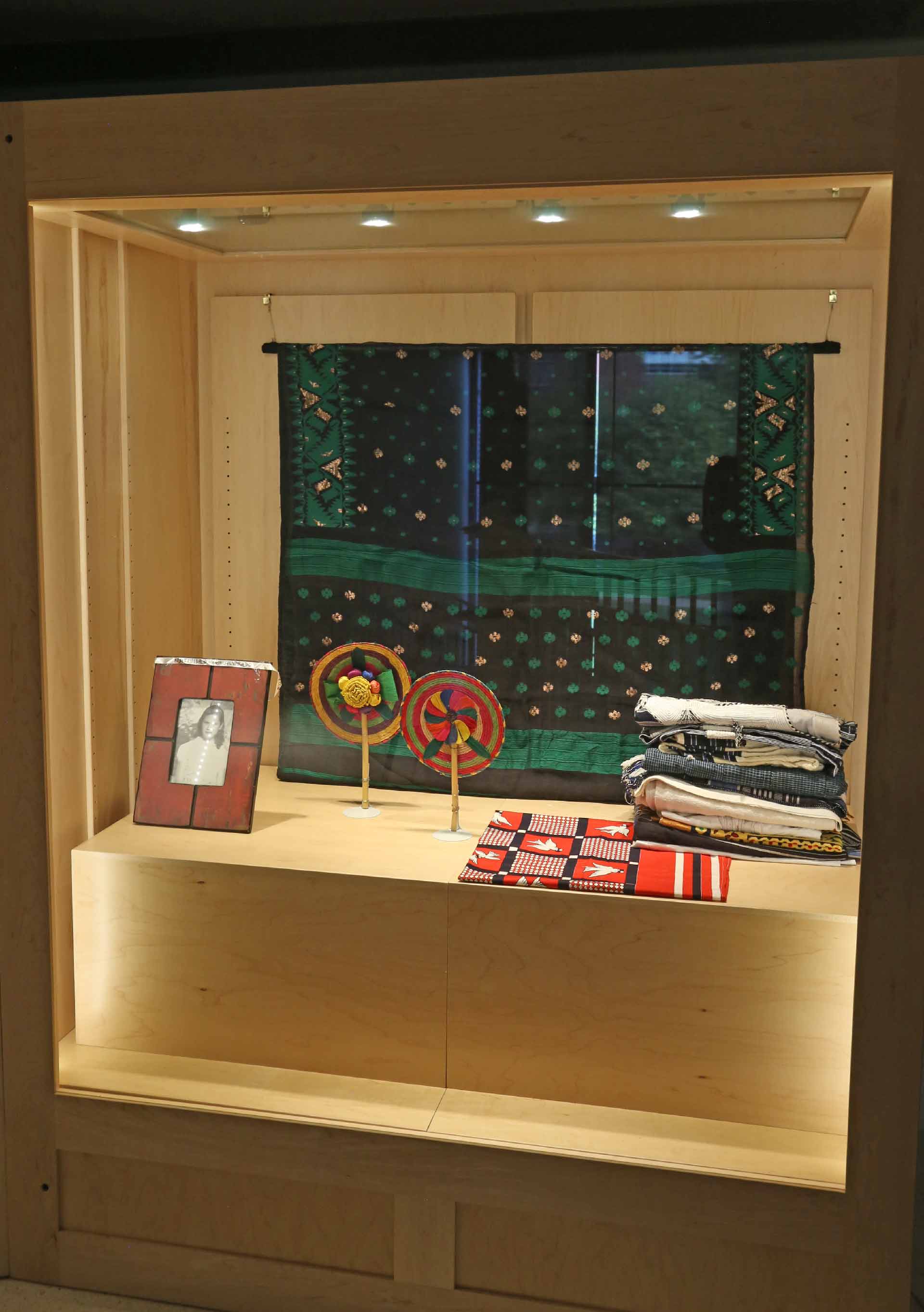 a shot of the second display case with the designed folded cloths, woven crafts and photo of a girl