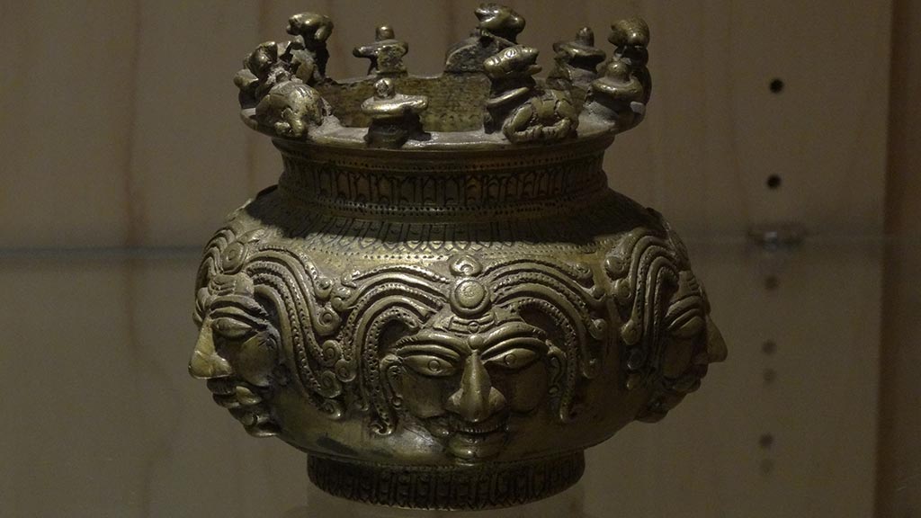 container with sculpted faces and figures on top