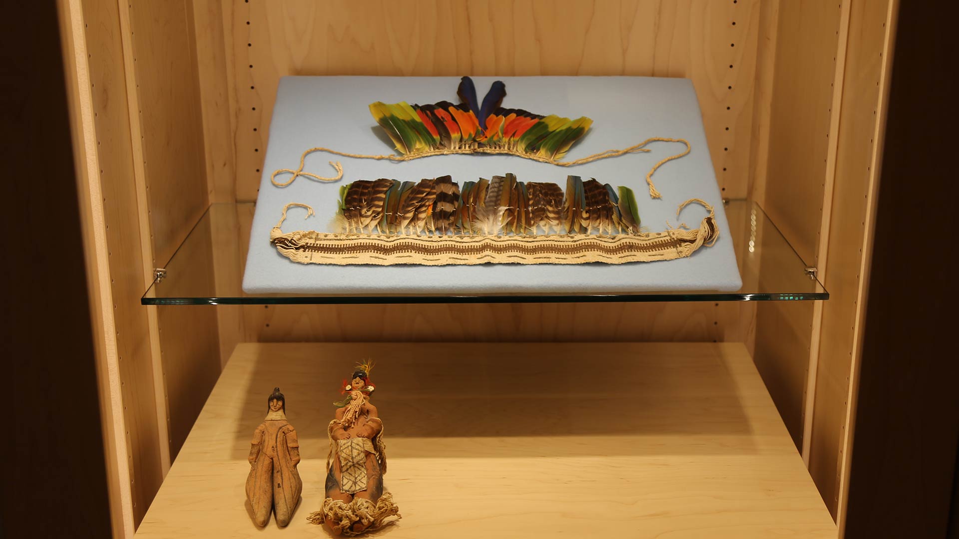 female and male dolls made of clay, headdress made of woven twine with multicolored feathers attached