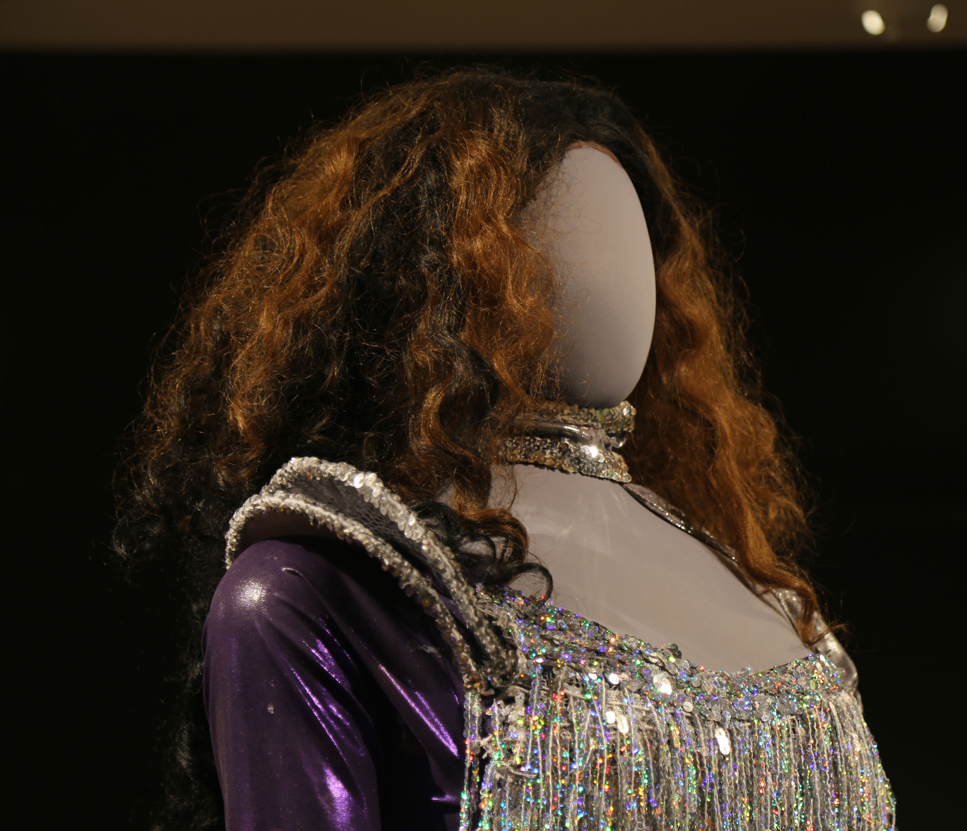 diagonal view of mannequin head with curly hair and sparkly costume with purple sleeves